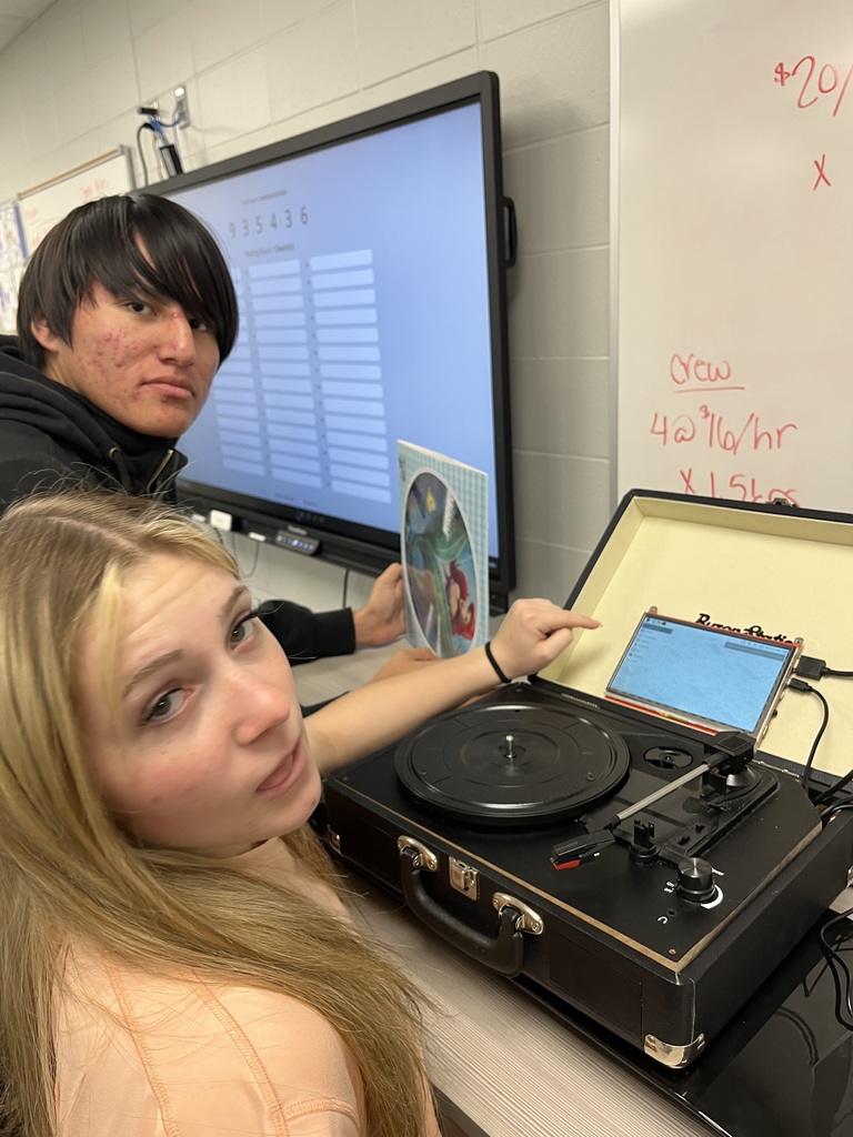 Two students work with a record player and computer during a classroom activity, examining the equipment and troubleshooting the technology.