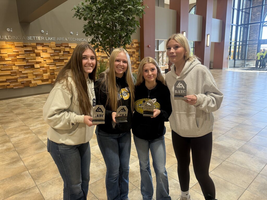 Four students pose together holding Lake Area Technical College awards inside the college's main lobby, celebrating their achievements during a technical education event.