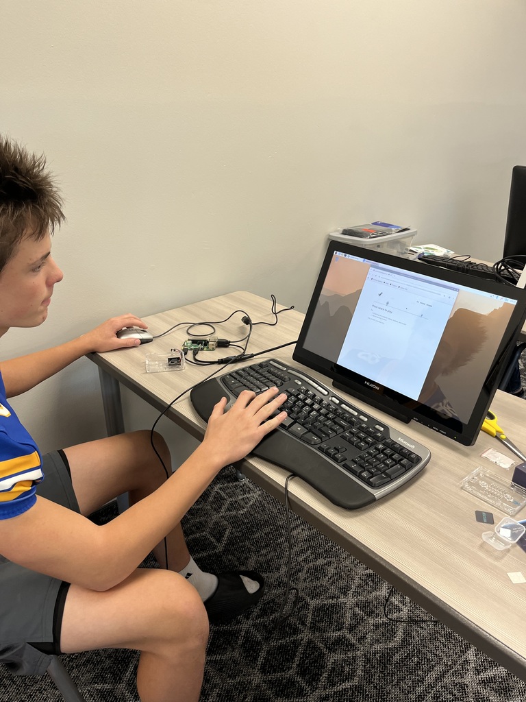 A student uses a Raspberry Pi computer connected to a monitor, keyboard, and mouse while following instructions during a hands-on computer science lesson.