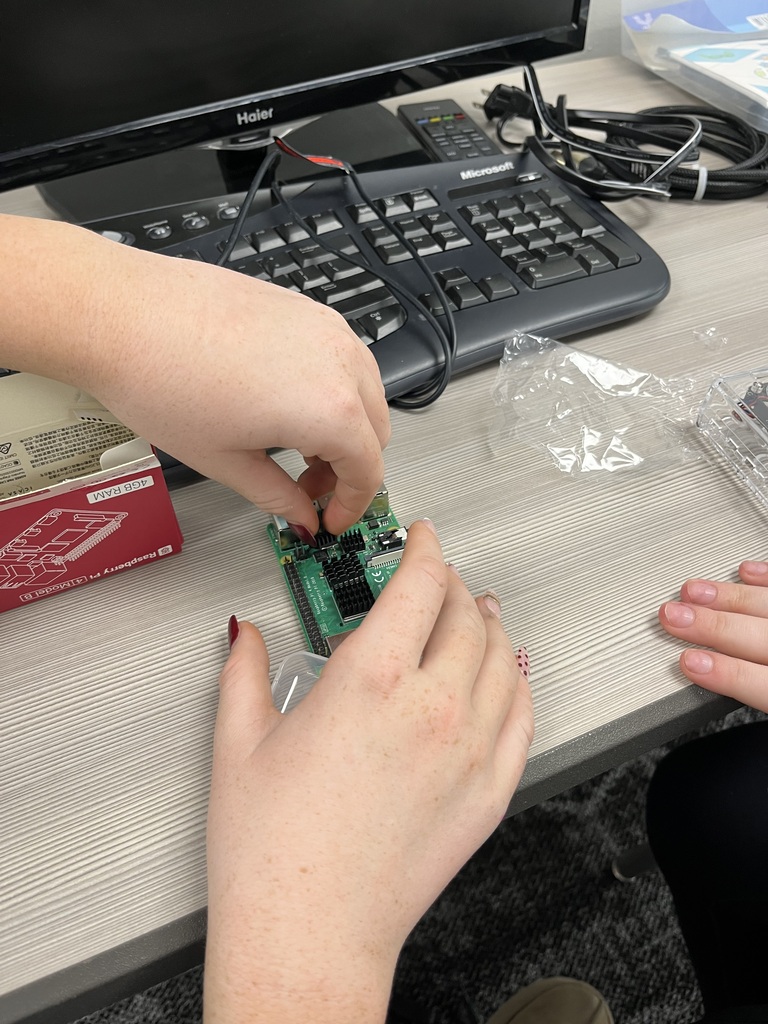 Close-up of students carefully installing small heat sinks onto a Raspberry Pi circuit board during a hands-on computer assembly activity.