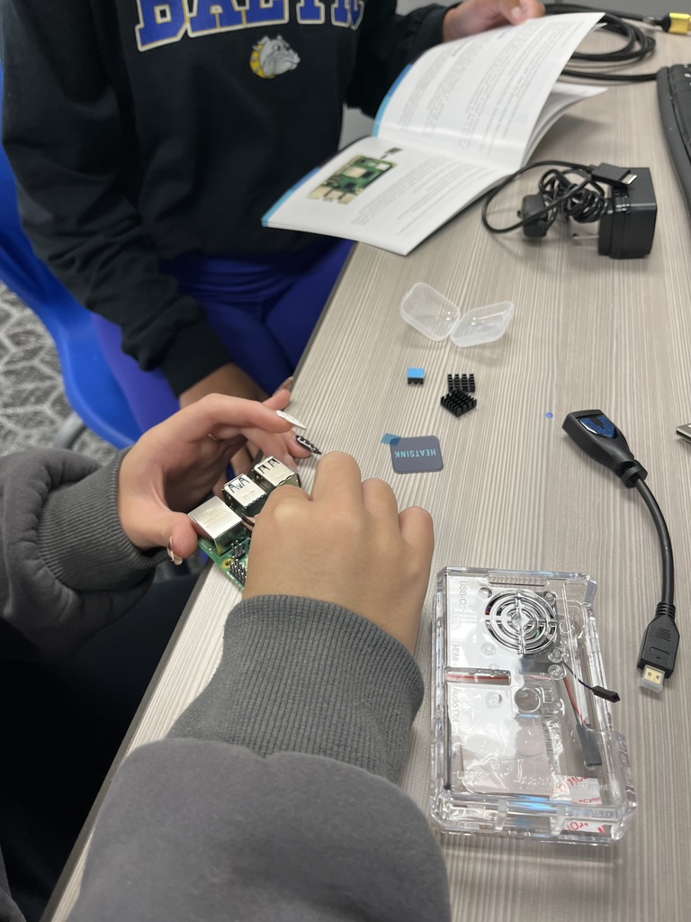 Students work together to assemble a Raspberry Pi computer, examining its ports and attaching components while referencing an instruction manual.