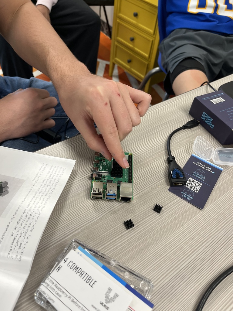 Close-up of a student's hand examining a Raspberry Pi 4 single-board computer, identifying its components and connections during a technology lesson.