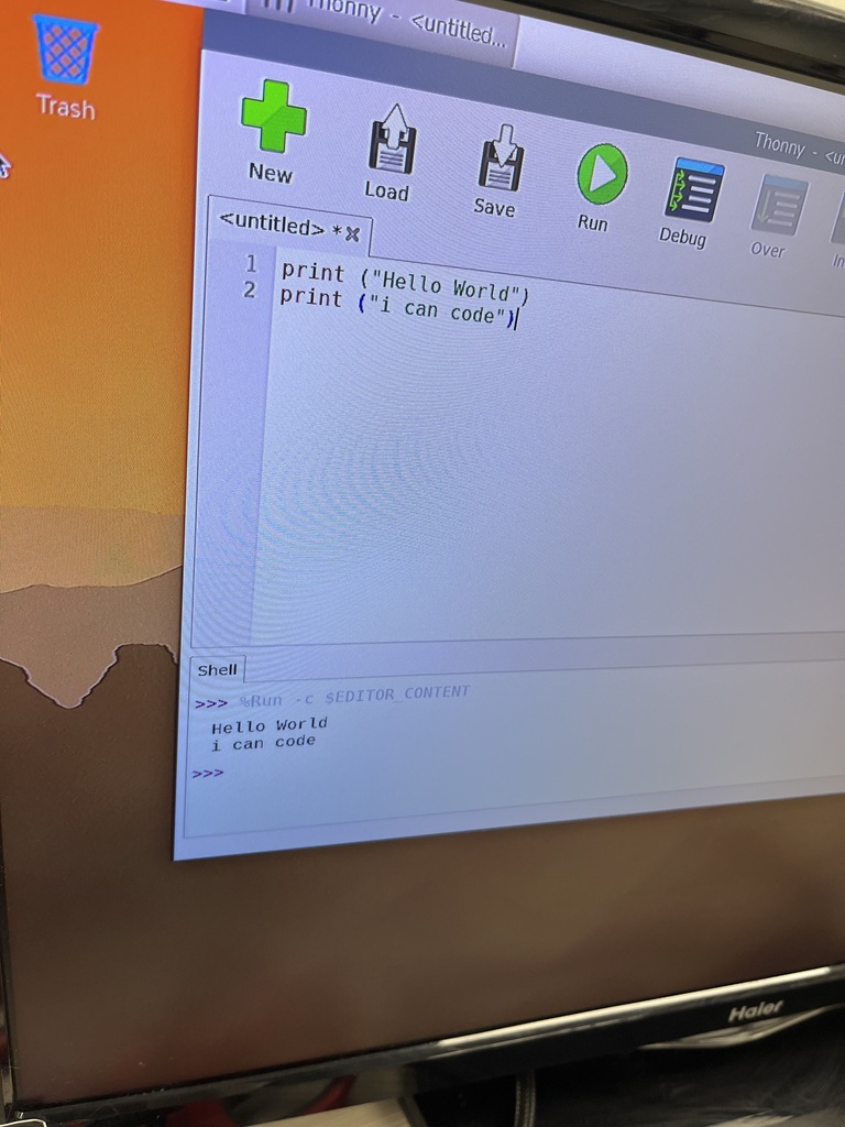 Close-up of a computer monitor displaying the Thonny Python programming environment. A student's first Python program successfully runs and displays the messages “Hello World” and “i can code” in the output window.