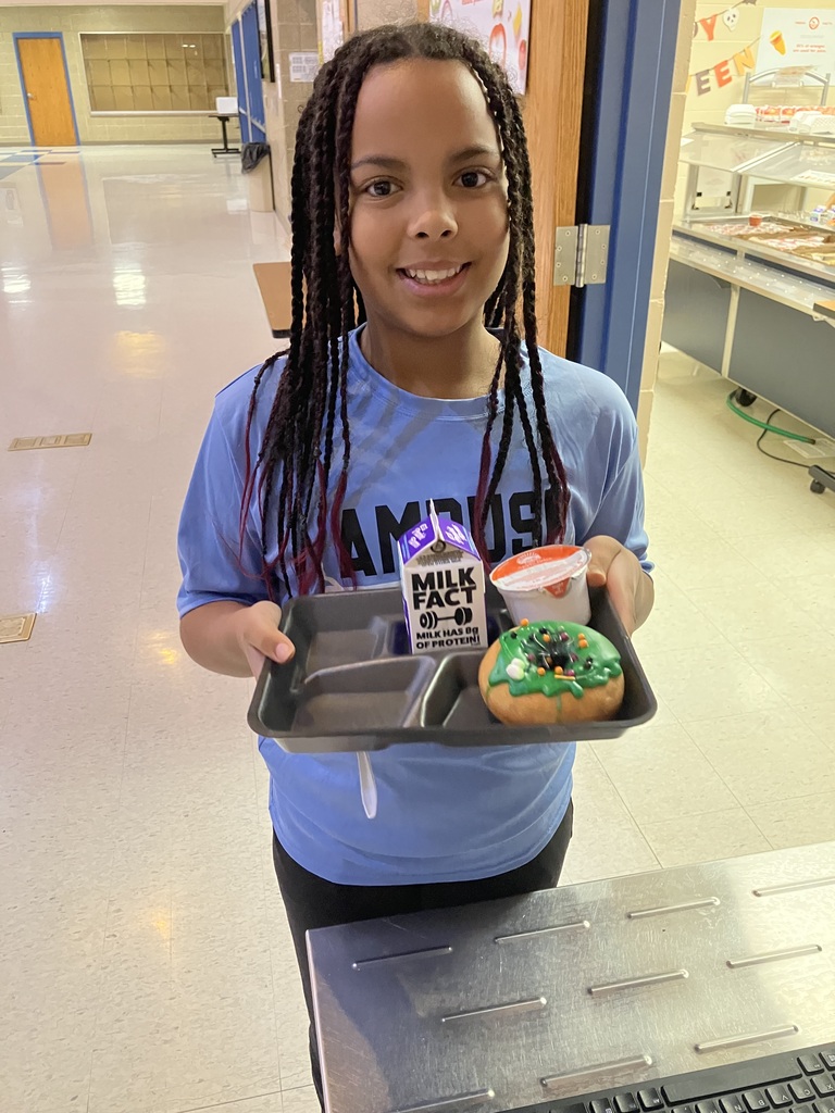A Baltic School District student smiles while holding a breakfast tray containing a green-frosted Halloween donut, milk, and other breakfast items during the Donuts with Grownups event.