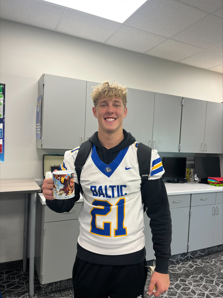 A Baltic School District student wearing a white Bulldogs football jersey with the number 21 smiles while holding a custom-designed ceramic mug featuring a colorful graphic.