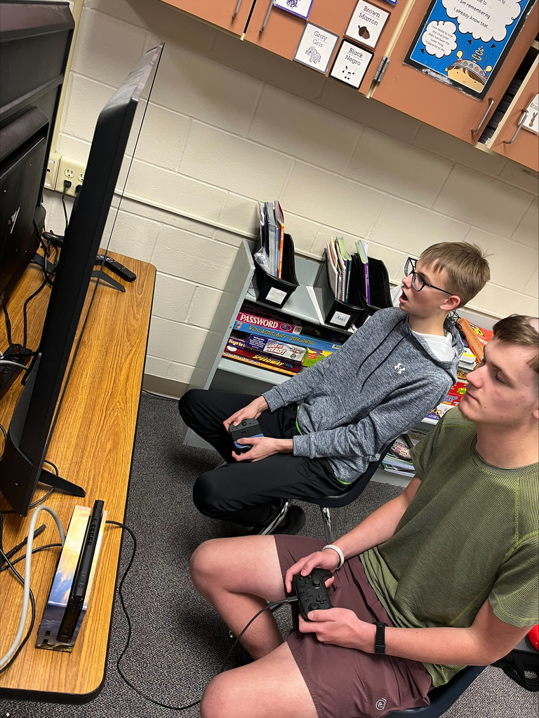 Two students participate in a Nintendo Switch gaming session, holding controllers and focusing on the television screen during an E-Sports activity.