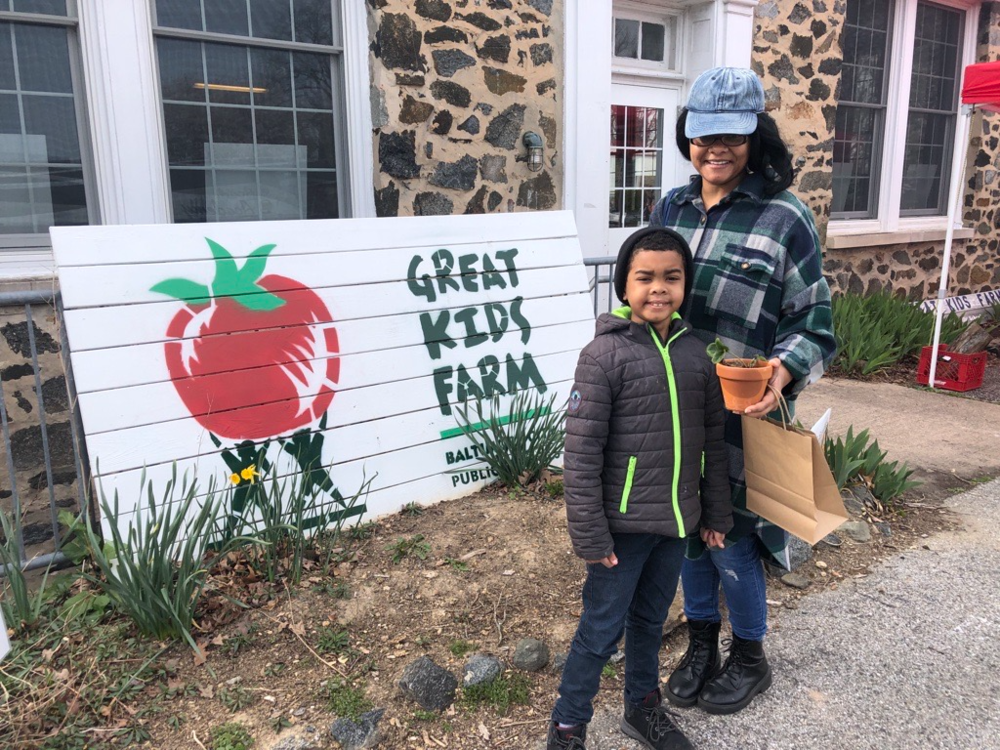 A parent and student stand in front of the Great Kids Farm sign outside