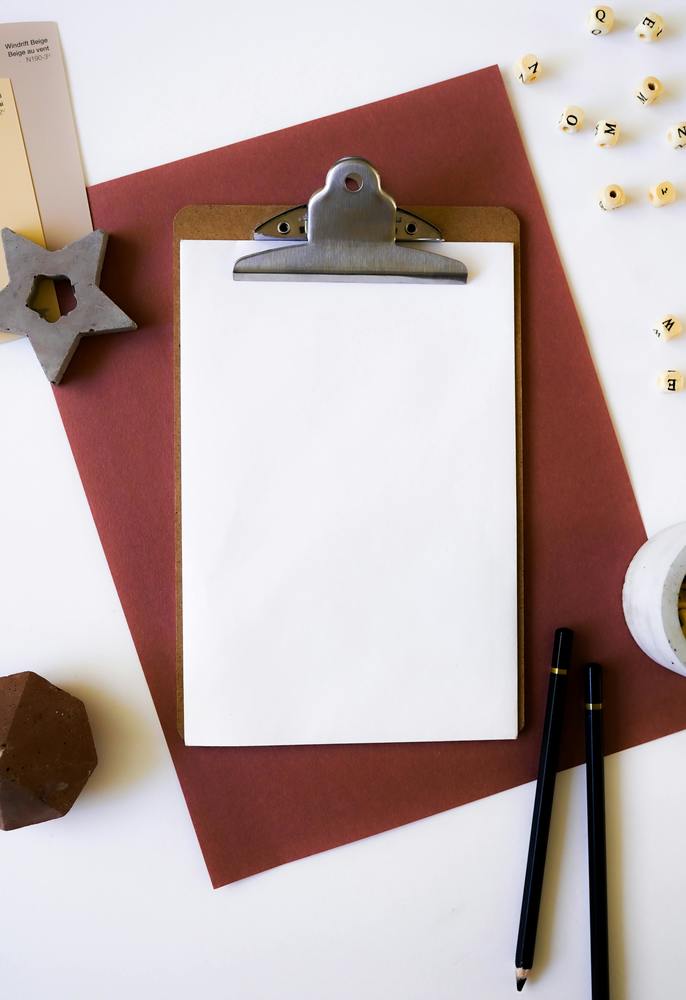 clipboard on a white desk surrounded by pencils, beads, and paper
