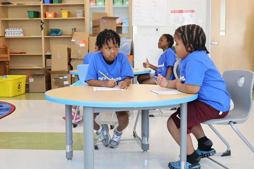 Students sit at a round table while discussing writing assignment.