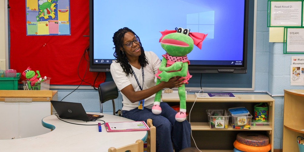 Teacher sitting in a chair holding a frog puppet