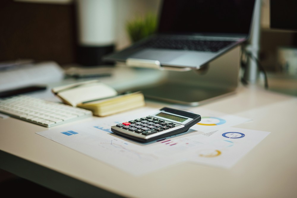 calculator on a desk with papers, a notebook, and a computer