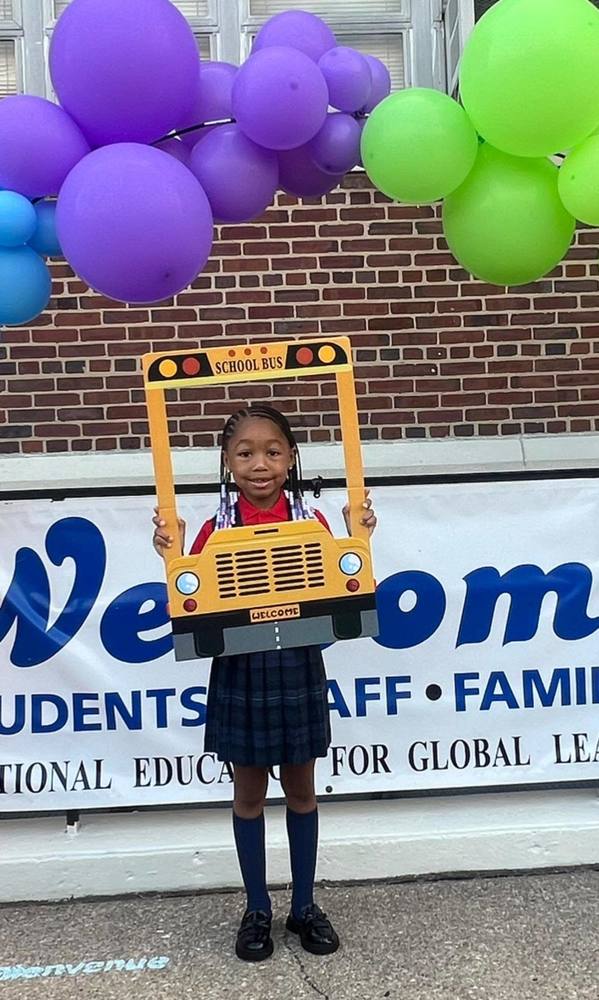 School student holds up a picture frame in the shape of a yellow school bus.