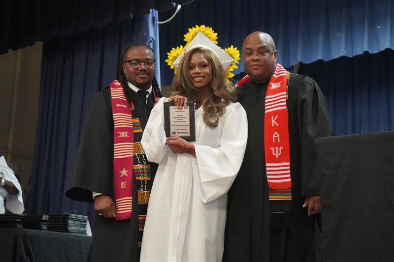 Graduating student posing with school leaders and holding her award