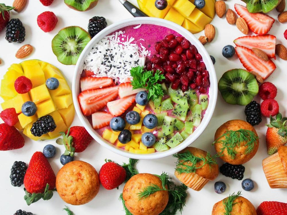 smoothie bowl with fruits as garnish and surrounded by fruits and muffins