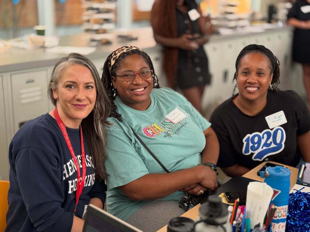 A photo of three smiling staff members sitting at a desk.