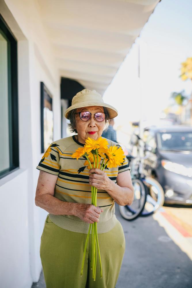 an older woman is holding and smelling flowers and smiling