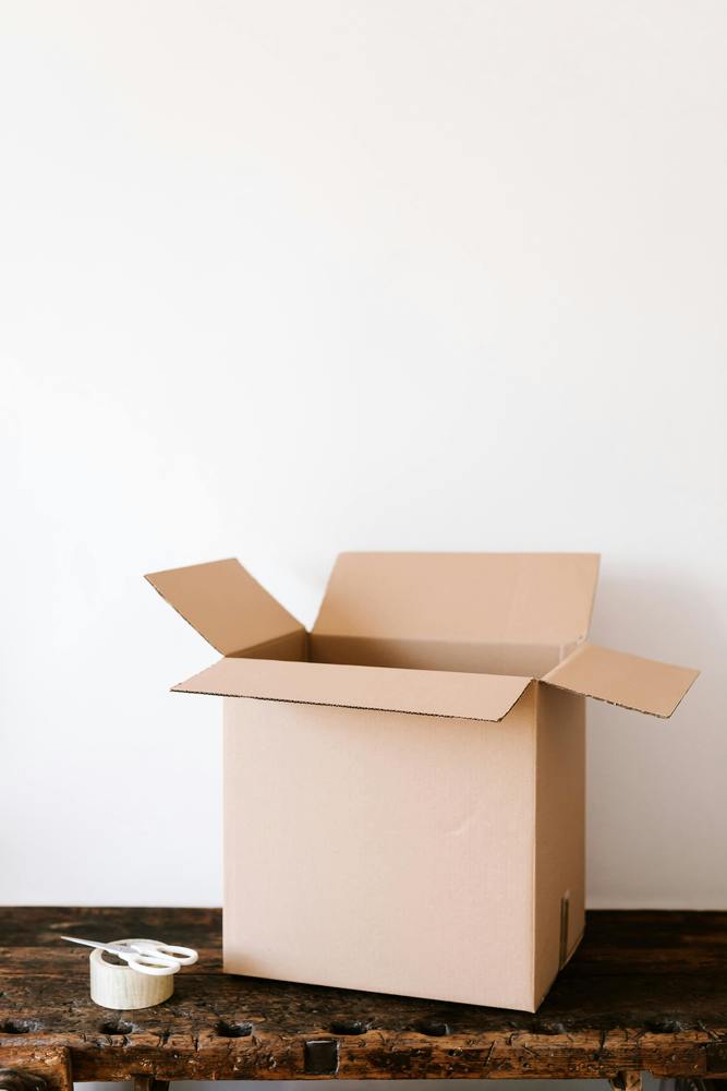 open cardboard box sitting on the floor next to a roll of packing tape and white scissors