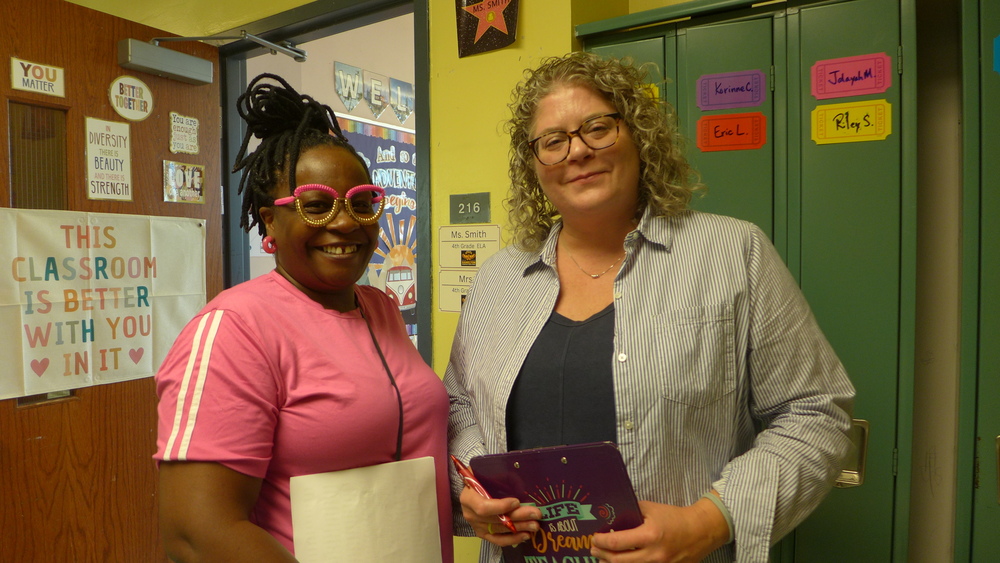 Two employees standing in front of a classroom doorway holding clipboards