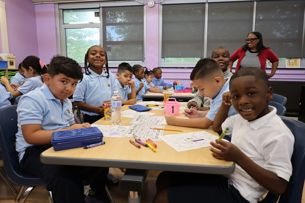 Students pose for a picture smiling at a desk.