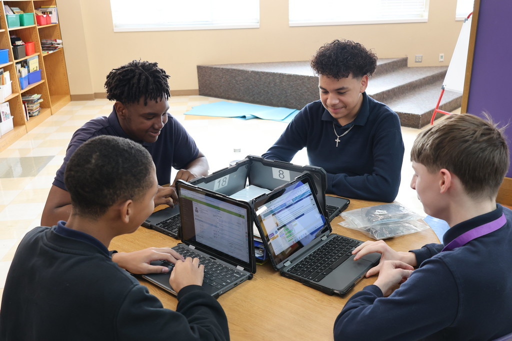 Four students sitting at a table typing on laptops