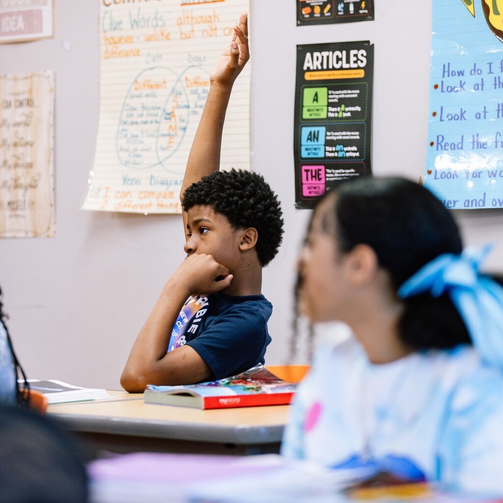 Student raising their hand while sitting at their desk