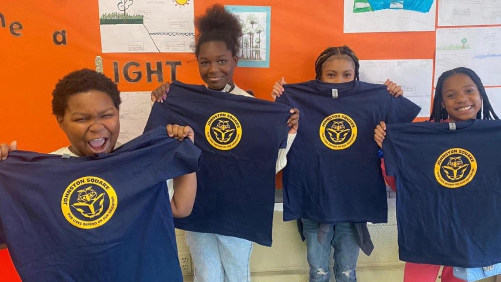 Student hold up shirts they won for perfect attendance
