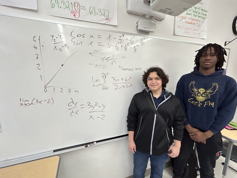 Oscar and Jordan pose for a photo up against a classroom whiteboard.