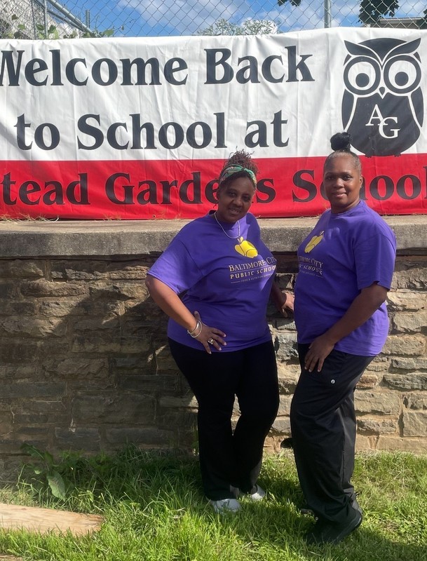 Food service staff members line up to take photo smiling in the cafeteria, all wearing matching shirts to celebrate the first day of school. 