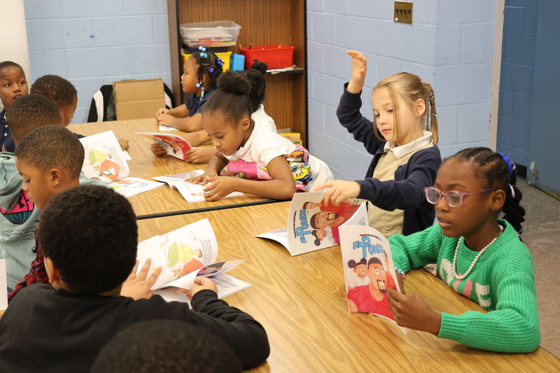 Students raise their hands in a read along activity.