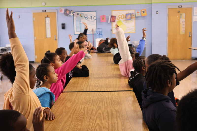 Students raise their hands in a read along activity. 