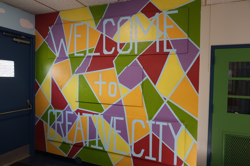 Welcome to Creative City mural is displayed to the right of the school's front entry doors. 