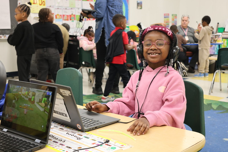 Student sits in front of a laptop while smiling at the camera.