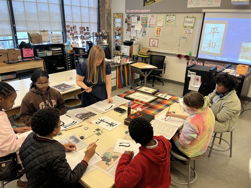 Jessica Chambers teaching Japanese calligraphy at a large table with students in a classroom setting