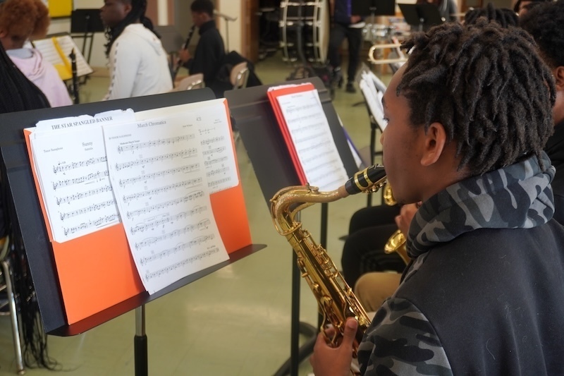 student playing a saxophone with sheet music in front of him on a stand 