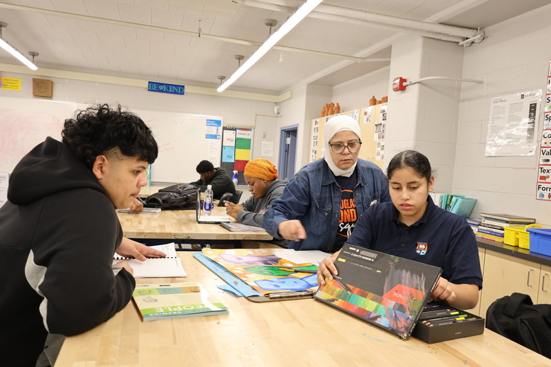 Art teacher assists student with chalk drawing on paper during class.
