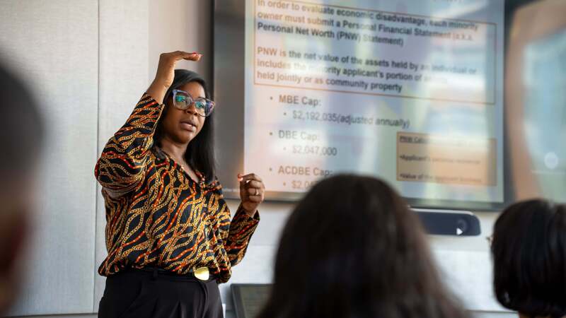 MWBE symposium presenter stands in the front of the room speaking.
