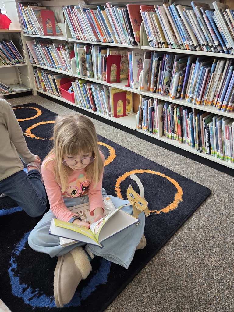 Members of the BHS Library Book Club visited two first-grade classes at Fourteenth Street, guided by Librarian Ms. Sprague. The purpose of the visit was to read aloud to the children and carry out a craft activity. They shared the book Dewey: There's a Cat in the Library by Vicki Myron and Brett Witter, which tells the heartfelt story of a real cat. As a kitten, Dewey was unfortunately dropped into a library's book return dropbox one night in Spencer, Iowa. The librarians decided to adopt him as the "library cat," allowing patrons to interact with him over the years. After the reading session, the first graders enjoyed coloring, cutting, and assembling their own library cats to take home and read to.