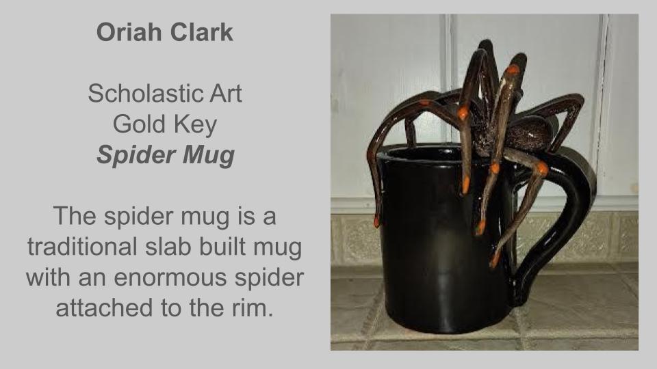 Mug with a large spider attached to the rim, on a tiled surface. Title reads "Scholastic Art Gold Key Spider Mug".