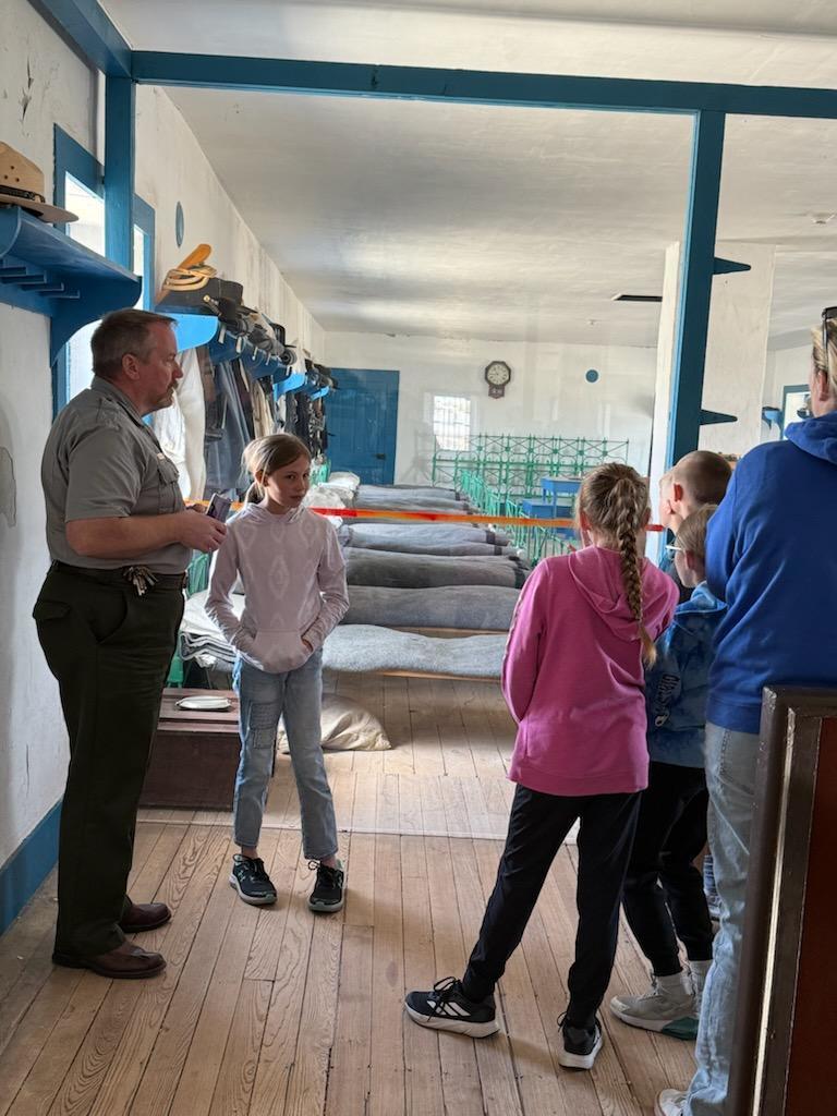 A series of photos showing Banner County students on a field trip to a historical museum or general store. Students are seen exploring vintage displays, looking at historical artifacts on wooden shelves, and gathered together in a rustic, wood-paneled building.