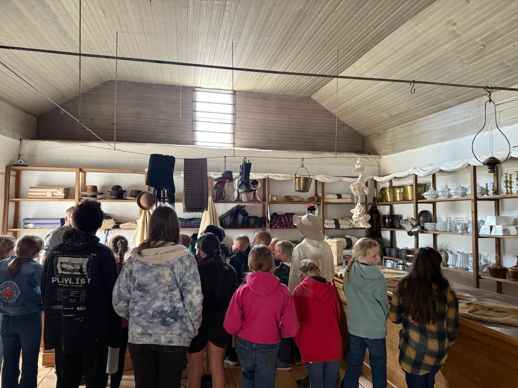 A series of photos showing Banner County students on a field trip to a historical museum or general store. Students are seen exploring vintage displays, looking at historical artifacts on wooden shelves, and gathered together in a rustic, wood-paneled building.