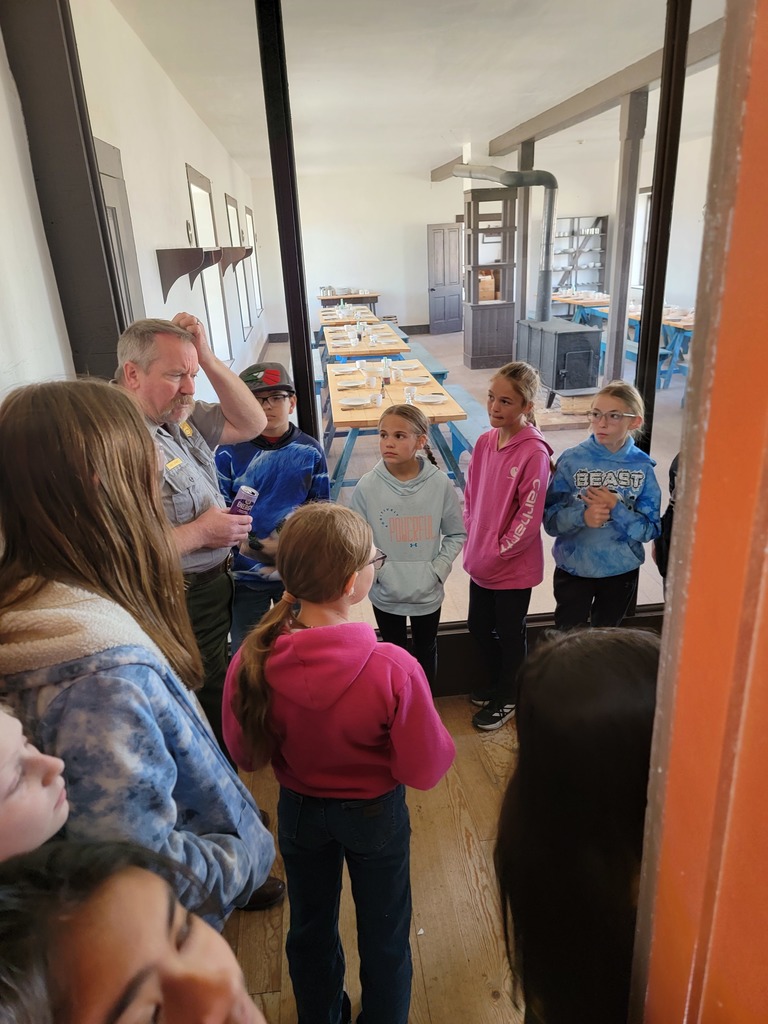 A series of photos showing Banner County students on a field trip to a historical museum or general store. Students are seen exploring vintage displays, looking at historical artifacts on wooden shelves, and gathered together in a rustic, wood-paneled building.