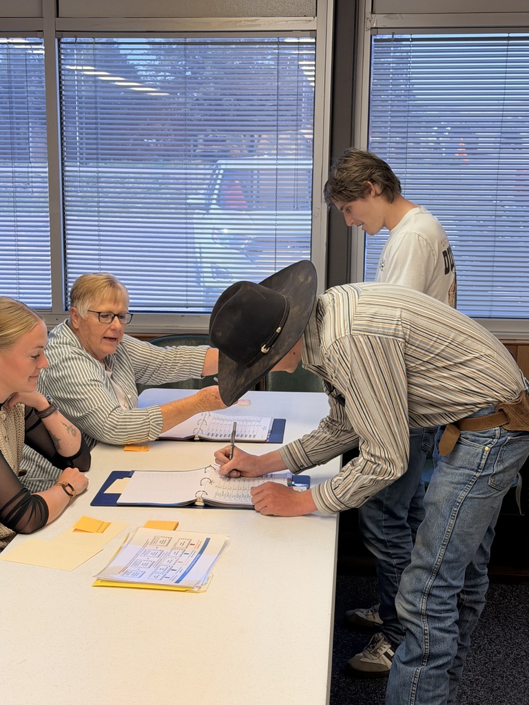 Two students and a staff member smiling and laughing together while signing papers at a table voting. 