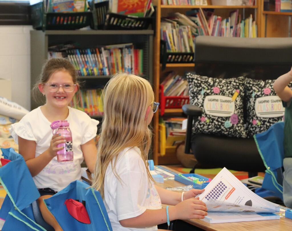 one student looking at the camera and one students flipping through a book