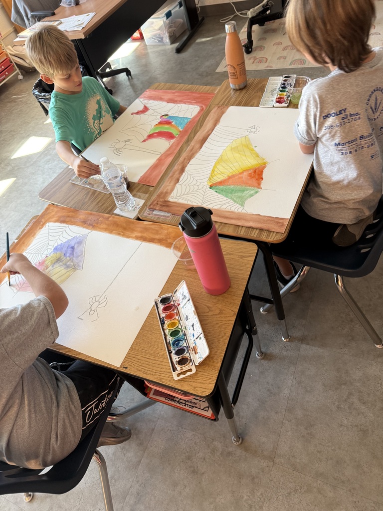 Elementary students sitting at classroom desks working on watercolor spiderweb art projects inspired by Charlotte's Web, using paintbrush trays and water cups.