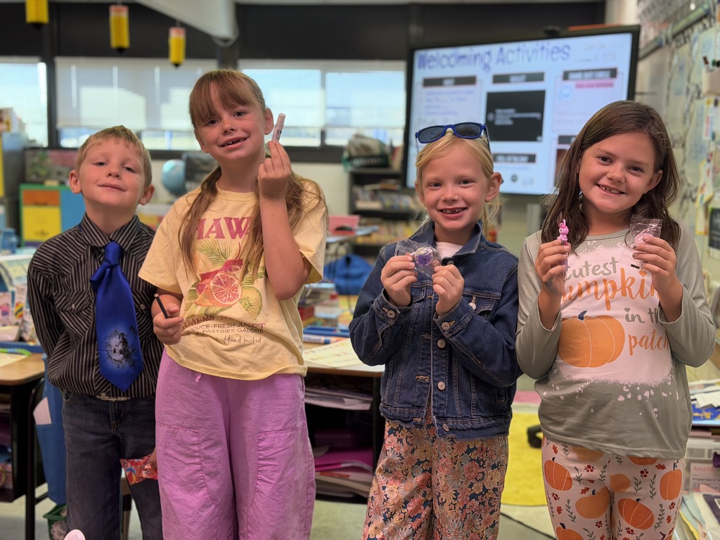 Four elementary students standing together in a classroom, smiling and showing off small crafts or decorated items they created.