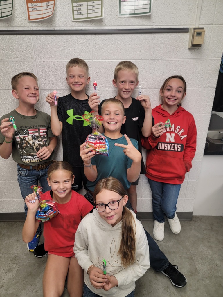 A group of seven elementary students posing together in a hallway, smiling and holding up small crafts and treats they made.