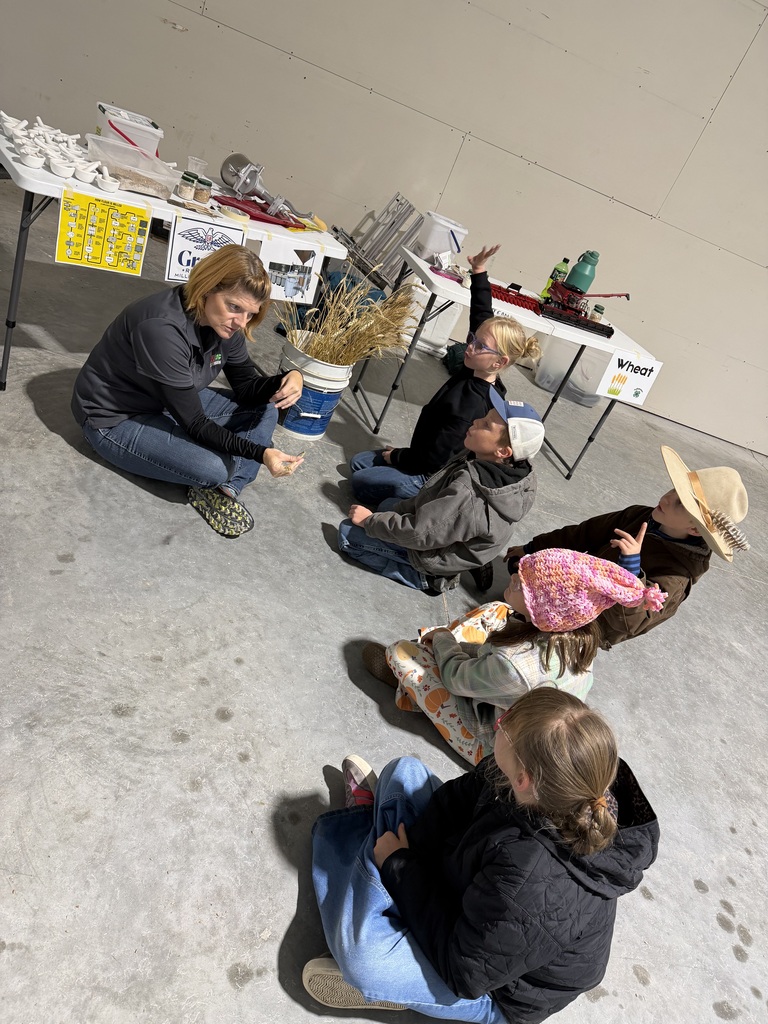 An instructor showing seeds to elementary students sitting on the floor during an agricultural learning presentation.