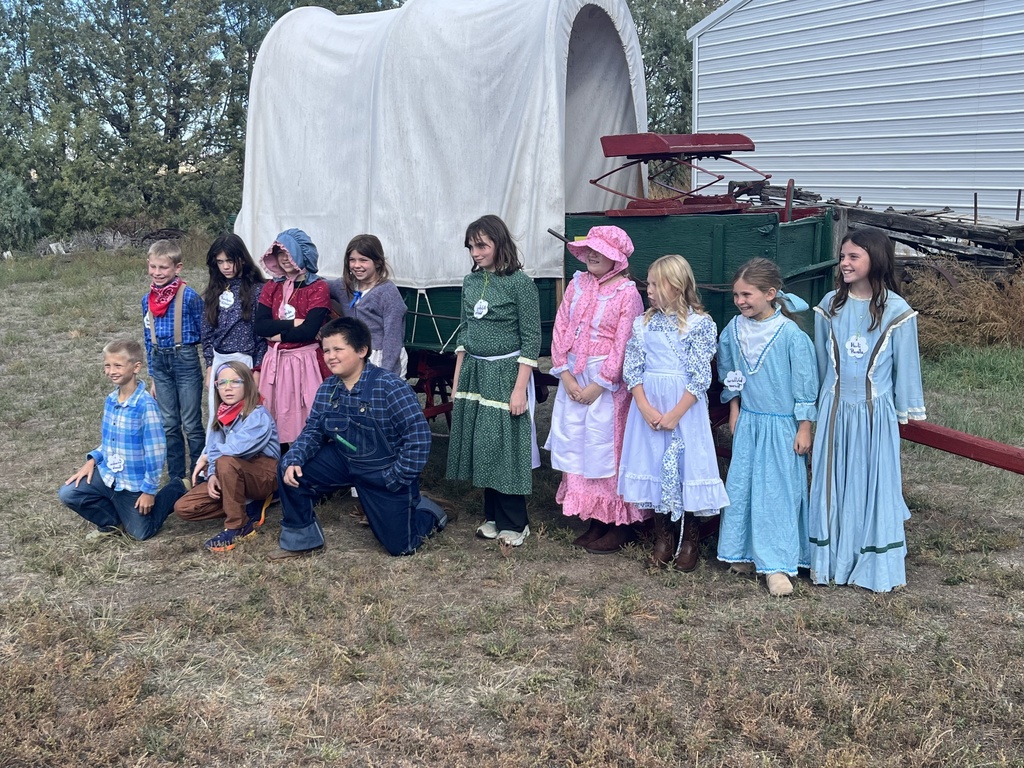 Students in pioneer costumes posing in front of a covered wagon.