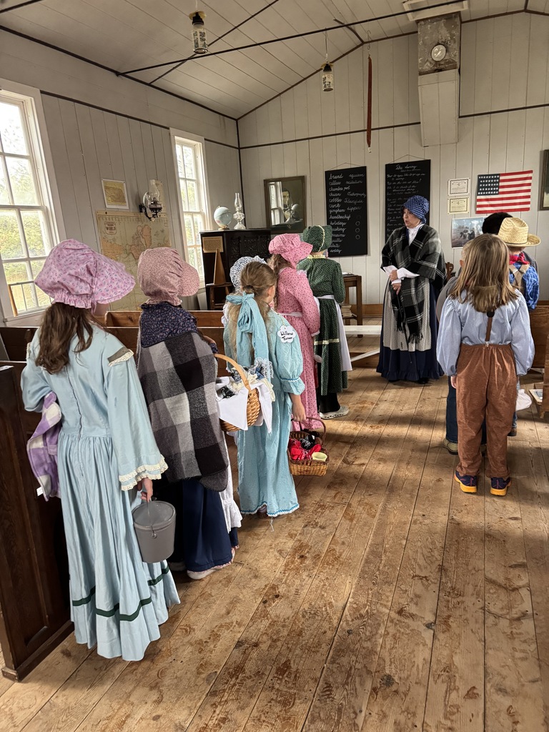 Elementary students in historic pioneer clothing and dresses standing on a wooden floor.