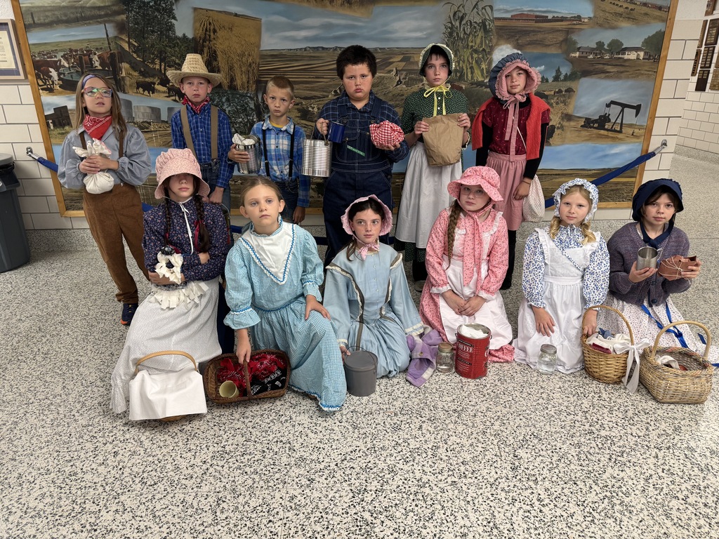 Elementary students in pioneer clothing posing outdoors in front of a painted mural.